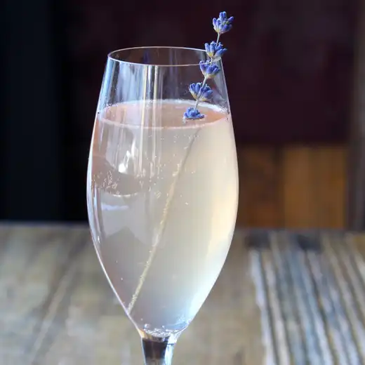 Pale sparkling cocktail in a flute glass garnished with a sprig of lavender