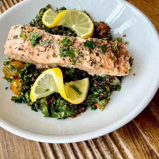 Seared salmon fillet with lemon slices over greens in a white bowl